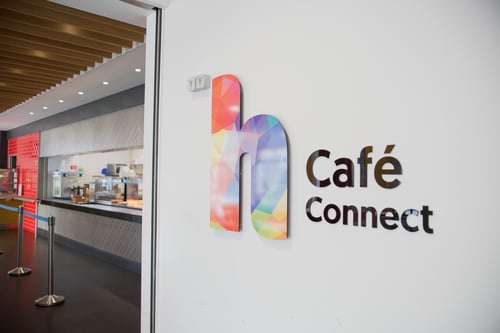 Entrance to Café Connect at Highlands College, featuring a modern interior with wooden ceiling panels, stainless steel kitchen equipment, and colourful branding.
