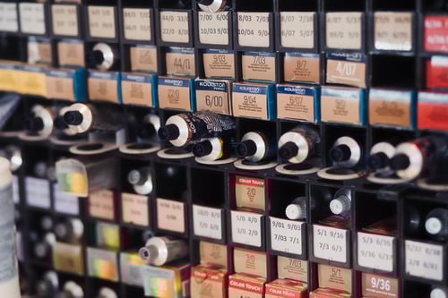 Organised shelf of hair color products at Highlands College, displaying labelled boxes and tubes sorted by shade codes for use in hairdressing training.