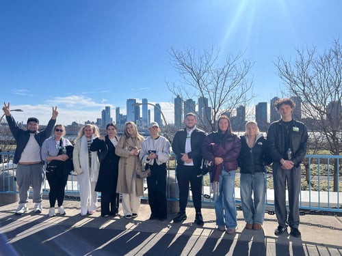 A medium shot of UCJ students outside with the New York City line in the background.