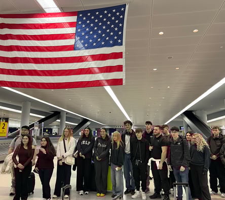 UCJ students in an airport in New York standing underneath an American flag.