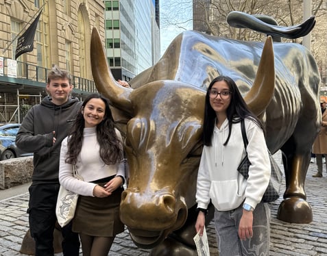 Students standing in front of a bronze bull during their visit to Wall Street on their New York trip.