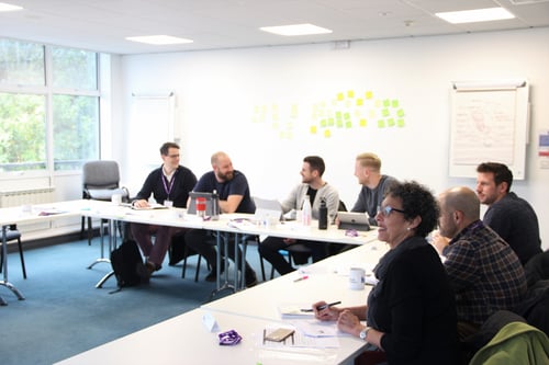 Highlands Professional students smiling and laughing with each other while sat at tables in classroom, with post it notes and whiteboards on the back wall