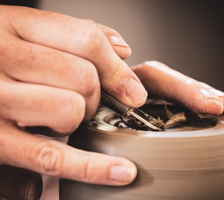 Hands on pottery wheel whilst carving into the top of a pot.
