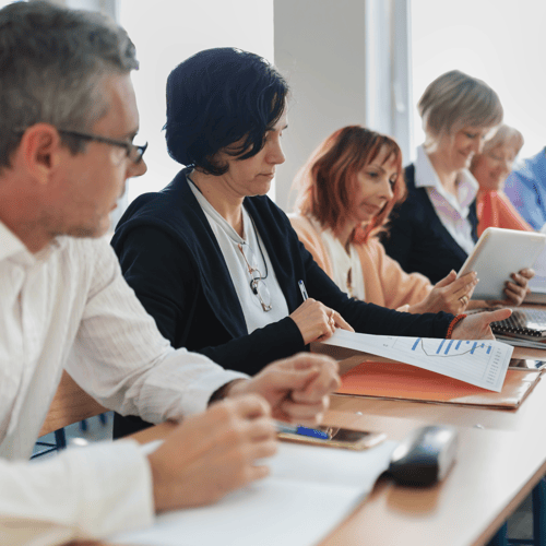 Adult learners sat in a row looking at paperwork on their table.