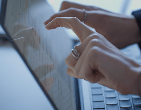 A medium close-up of two hands about to touch the screen of a laptop covered in text.